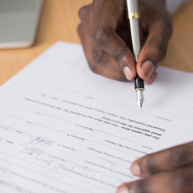 Close-up of a man's hands signing a formal document indoors.